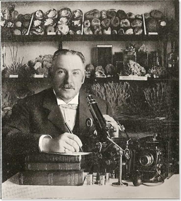 Edward Connold sitting at a desk with a microscope surrounded with natural history paraphernalia